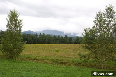 Panoramic view of a mountainous landscape with a lake or river in the foreground, showcasing the rugged beauty of Northern New Hampshire.