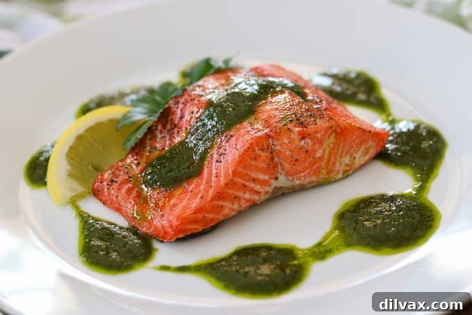 A perfectly cooked salmon fillet, generously topped with a vibrant green chimichurri sauce, ready to be served.