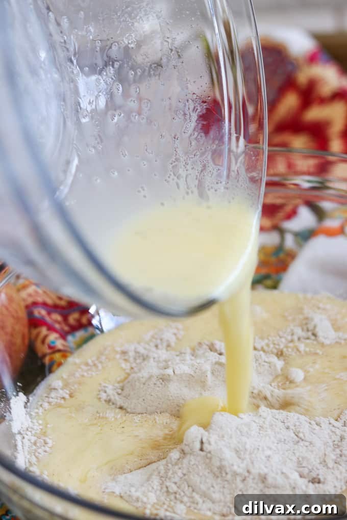 Pouring the wet ingredients into the dry ingredients to make Apple Streusel Muffins. Mixing the wet ingredients into the dry ingredients for Apple Streusel Muffins, demonstrating a crucial step in batter preparation.