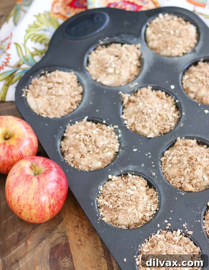 Apple Streusel Muffins before going into the oven. Unbaked Apple Streusel Muffins generously topped with a golden streusel, perfectly arranged in a muffin tin, ready to go into the oven for baking.