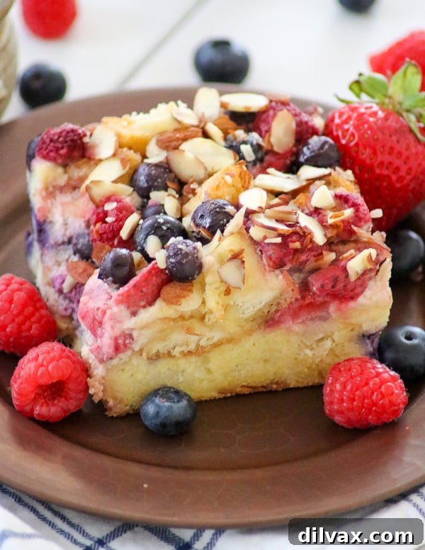 A beautifully composed shot of Almond Berry French Toast Casserole surrounded by an abundance of fresh blueberries, raspberries, and strawberries, highlighting the vibrant fruit.