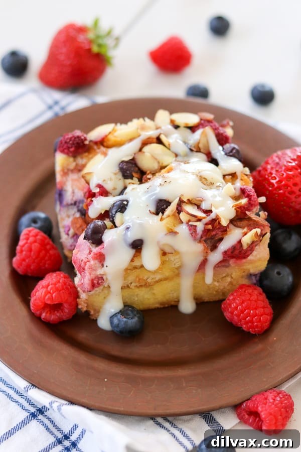 A close-up of a generous slice of Almond Berry French Toast Casserole, beautifully plated and liberally drizzled with Grandma's Waffle Sauce, showcasing its decadent appeal.