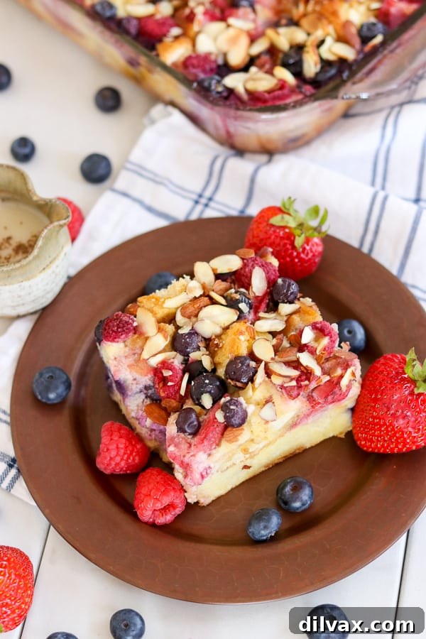 A perfectly portioned slice of Almond Berry French Toast Casserole served on a plate with a small bowl of waffle sauce on the side for dipping.