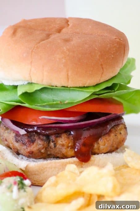 A Cheesy Spiced Pork Burger topped with fresh lettuce, a slice of ripe tomato, crisp red onion, and a drizzle of tangy BBQ sauce.