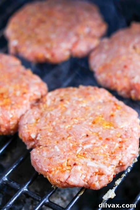 Cheesy Spiced Pork Burgers cooking on the grill, showing a good sear and juicy texture.