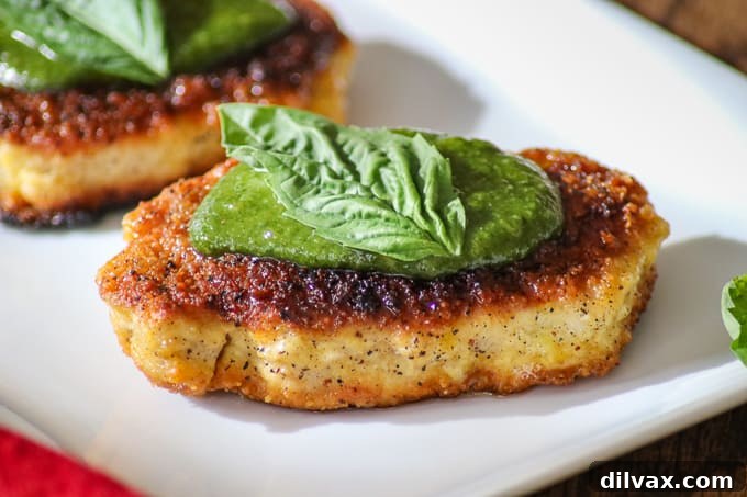 Parmesan Pork Chops with Pesto on a pristine white plate, garnished with fresh basil leaves, ready to be served.