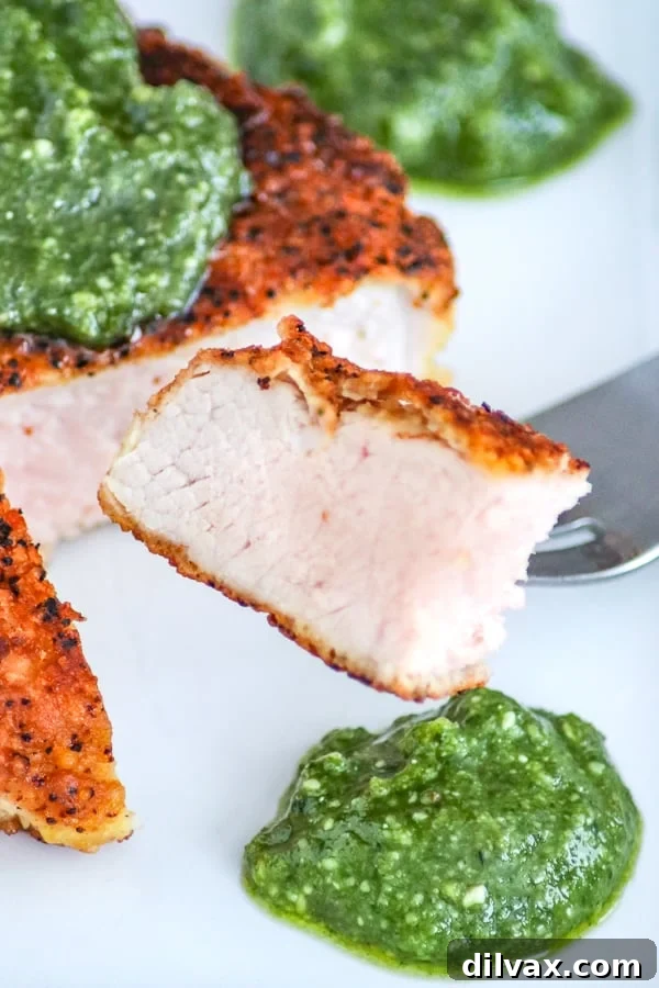 A close-up of a piece of Parmesan Pork Chop with Pesto on a fork, showing the tender, slightly pink interior.