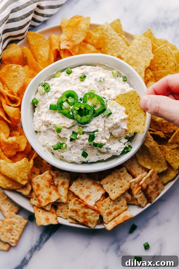 Jalapeño Ranch Dip in a bowl surrounded by chips and crackers. A pristine, creamy bowl of Jalapeño Ranch Dip, beautifully presented and surrounded by an enticing selection of tortilla chips and savory crackers. The dip's smooth texture and subtle green highlights invite immediate indulgence, making it a perfect appetizer. The image captures the fresh appeal and readiness for any social gathering.