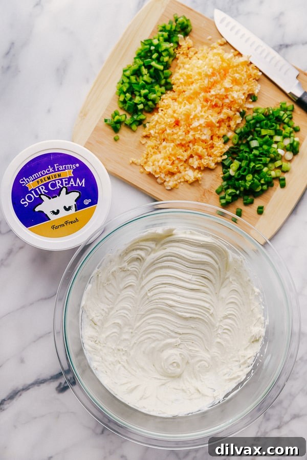 Making Jalapeño Ranch Dip with Shamrock Farms Sour Cream. A close-up shot of the Jalapeño Ranch Dip being prepared, with a spatula gently folding in diced jalapeños and shredded cheese into the creamy base of Shamrock Farms Sour Cream. The process highlights the ease of mixing and the fresh ingredients coming together to form a delicious appetizer. The focus is on the rich, inviting texture of the dip in its making.