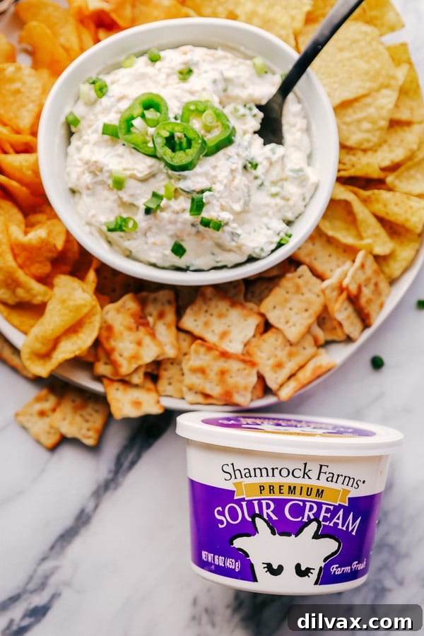 Crackers, Chips, Jalapeño Ranch Dip and Shamrock Farms Sour Cream. An inviting overhead shot displaying a beautiful spread: a bowl of creamy Jalapeño Ranch Dip takes center stage, generously surrounded by an assortment of crispy crackers and crunchy tortilla chips. In the background, a container of Shamrock Farms Sour Cream subtly highlights the premium ingredient used in the dip, making this a perfect, fresh arrangement for sharing.