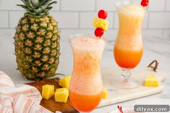 Paradise Blend 2 Two glasses of vibrant Frozen Bahama Mamas garnished with pineapple and cherries, set against a blurred tropical background.