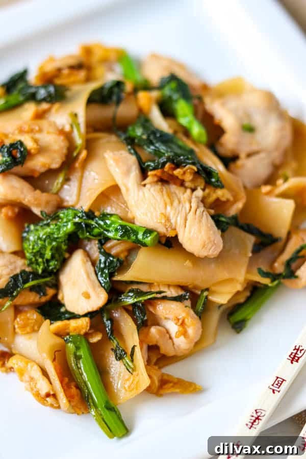 Close up of Pad See Ew on a plate with chopsticks, showing texture and ingredients.