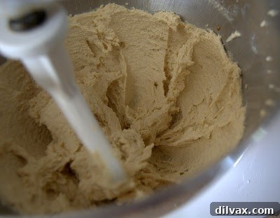A close-up of an egg and vanilla extract being added to the creamed butter and sugar mixture in a stand mixer.
