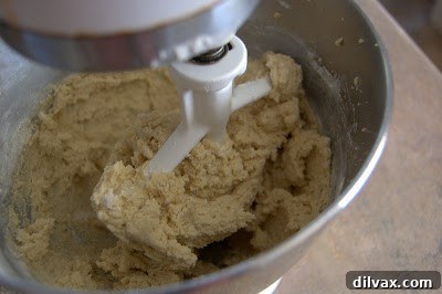A spatula gently folding white chocolate chips into the prepared cookie dough in a mixing bowl, ensuring even distribution.