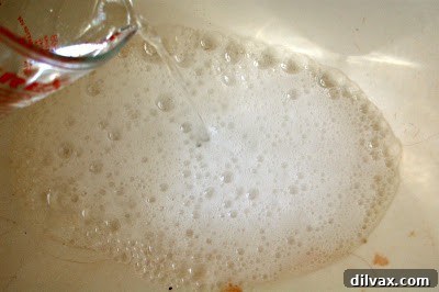 Close-up of the active fizzing and bubbling chemical reaction between baking soda and vinegar in the sink drain.