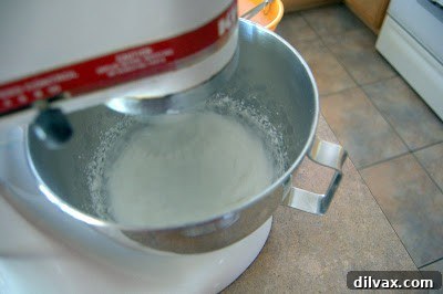 Sugar being gradually added to whipping egg whites in a stand mixer.