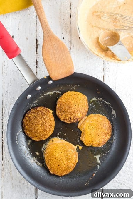 Hearty Pumpkin Wheat Stack 9 Two pumpkin pancakes cooking side-by-side on a hot griddle.