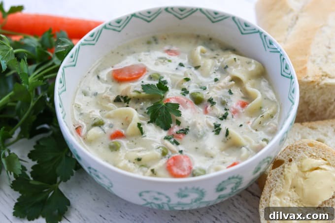 A steaming bowl of creamy homemade chicken noodle soup with tender chicken, noodles, peas, and carrots, garnished with fresh parsley.