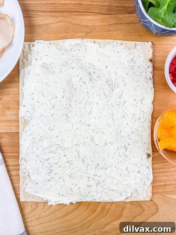 The creamy, dill-infused cream cheese layer spread generously on a lavash, ready for the other wrap ingredients.
