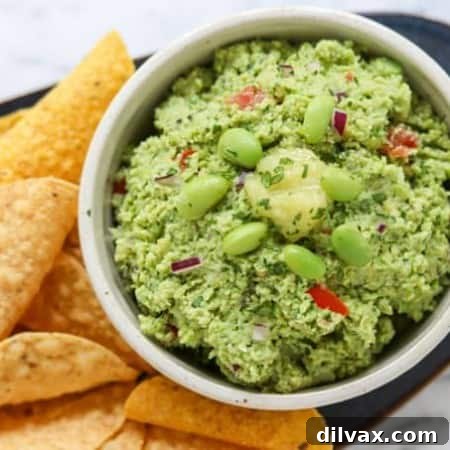 A bowl of guacamole with edamame and ginger surrounded by chips.