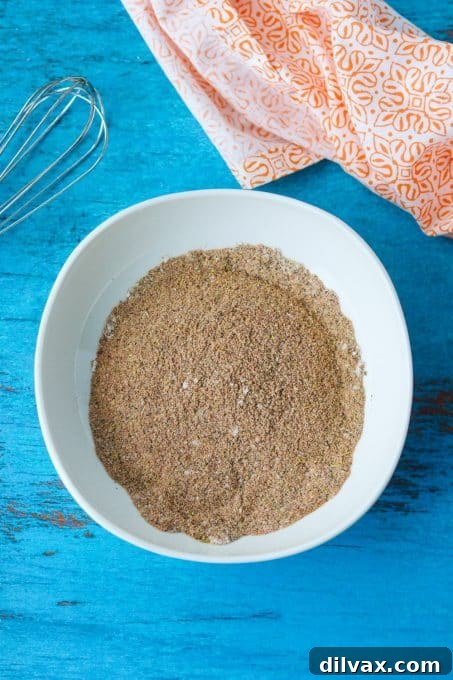 DIY Taco Spice Blend 5 A spoonful of rich, homemade taco seasoning with various whole and ground spices in the background.