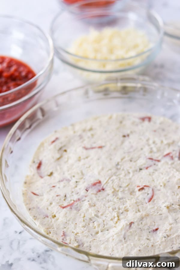 Pepperoni in the cheese layer of a dip. Close-up of the cheese layer mixed with pepperoni quarters, prior to baking.