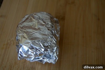 Garlic head securely wrapped in aluminum foil, ready for roasting.