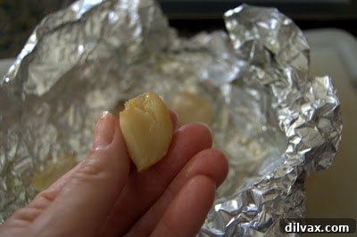 Close-up of roasted garlic cloves being gently squeezed from their skins.