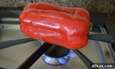 Red bell pepper charring over an open flame on a gas stove burner.