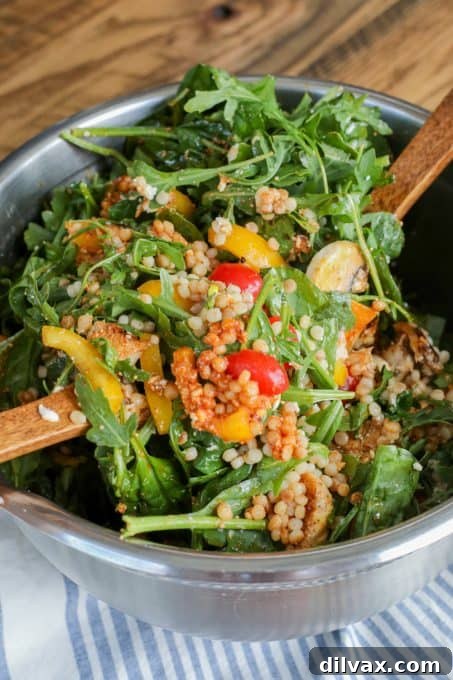 Tossing an Israeli Couscous Chicken Salad with a wooden spoon.
