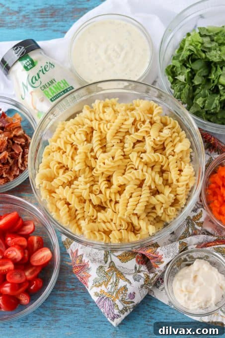 Fresh ingredients laid out for a Ranch Pasta Salad, including pasta, bacon, tomatoes, and Marie's Creamy Ranch Dressing.