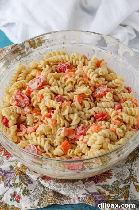 A bowl of pasta salad covered with plastic wrap, ready for refrigeration.