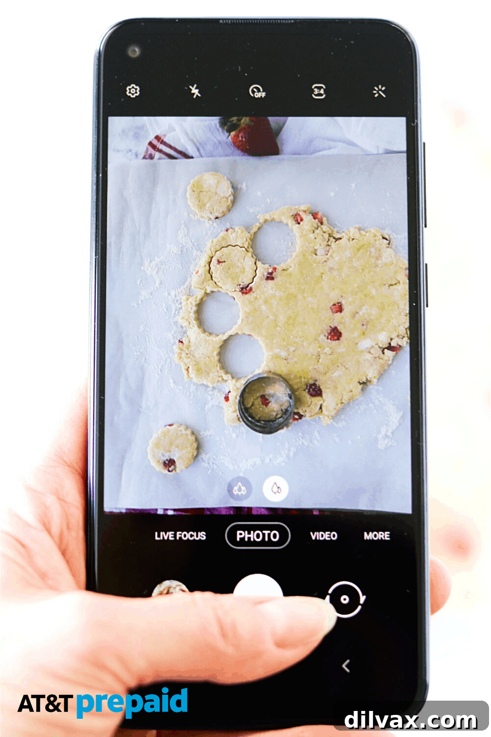 A close-up of scone dough being gently pressed and cut on a floured surface, with an AT&T PREPAID Samsung phone visible in the background, illustrating seamless integration of technology and daily life.