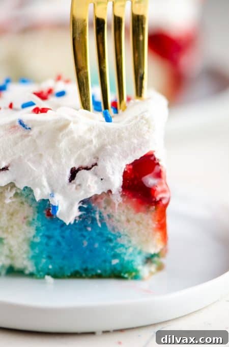 A fork digging into a colorful slice of red, white, and blue poke cake, revealing the distinct layers.