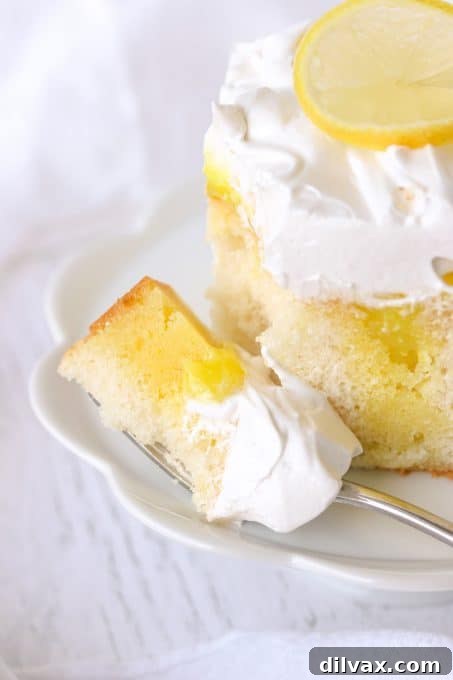 A tantalizing close-up of a bite of Lemon Marshmallow Poke Cake on a fork, showing the moist cake and fluffy frosting.