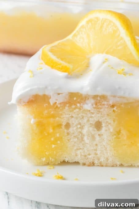 A close-up of a slice of Lemon Poke Cake showing the distinct layers and moist texture.