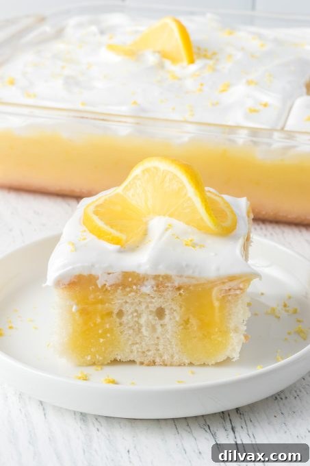 A beautiful slice of Lemon Poke Cake with distinct layers of lemon gelatin, lemon curd, and fluffy marshmallow frosting.