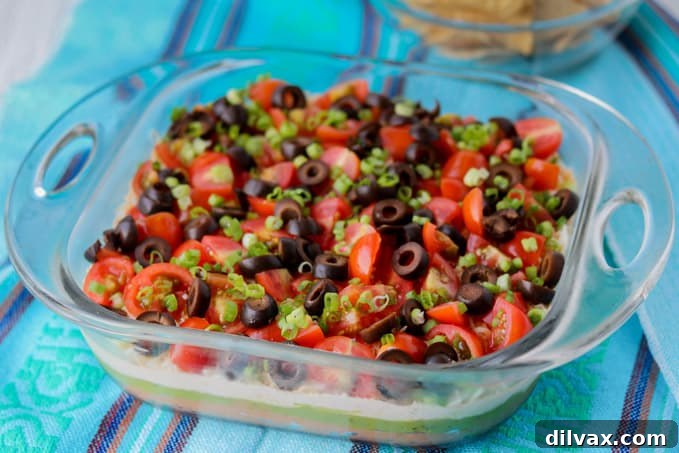Beautifully layered 7-Layer Dip with beans, guacamole, sour cream, tomatoes, olives, green onions, and cheese, ready to be served.