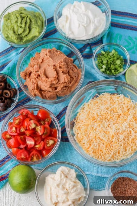 A selection of fresh ingredients laid out for making 7-Layer Dip, including tomatoes, olives, green onions, and cheese.