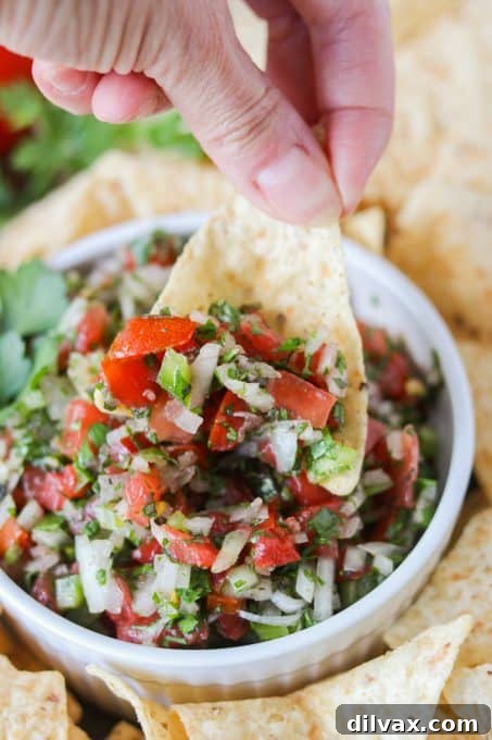 A hand dipping a tortilla chip into a large bowl of fresh veggie salsa.