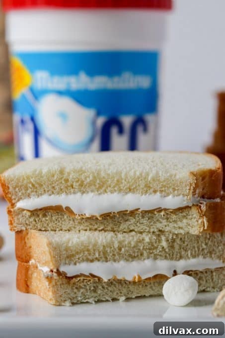 Effortless Fluffernutter Bliss 5 Two slices of white bread on a cutting board, with a knife used to spread creamy peanut butter on one slice and a dollop of marshmallow fluff on the other, ready for assembly.