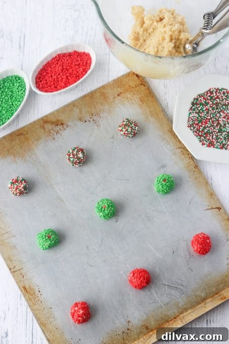 Unbaked balls of Christmas cookies, rolled in sprinkles, arranged on a parchment-lined baking sheet.