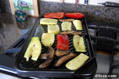 A medley of sliced vegetables, including zucchini and bell peppers, actively grilling on a hot grill pan, visibly developing distinct char marks and softening as they cook.