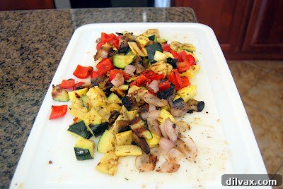 A close-up view of cooled grilled vegetables being skillfully cut into uniform, bite-sized pieces on a sturdy cutting board, preparing them for incorporation into the salad.