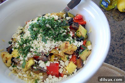 A generous sprinkling of crumbled feta cheese and finely chopped fresh flat-leaf parsley being added to the vibrant mixture of orzo pasta and grilled vegetables in a large bowl.