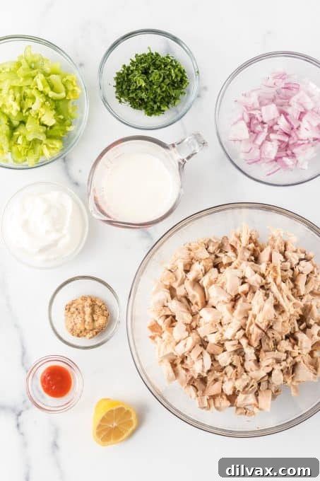 Ingredients for Chicken Salad without Mayo. A colorful display of fresh ingredients including cooked chicken, celery, red onion, parsley, Greek yogurt, buttermilk, mustard, and hot sauce.