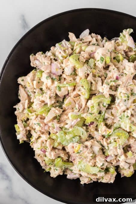 A bowl of chicken salad made without mayonnaise. A close-up view of the finished chicken salad in a white bowl, showing its creamy texture and visible pieces of chicken and vegetables.