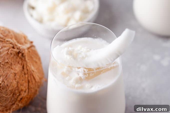 Tropical Coconut Bliss 2 A glass full of a creamy coconut drink garnished with a fresh coconut slice and straw, evoking a tropical vacation.