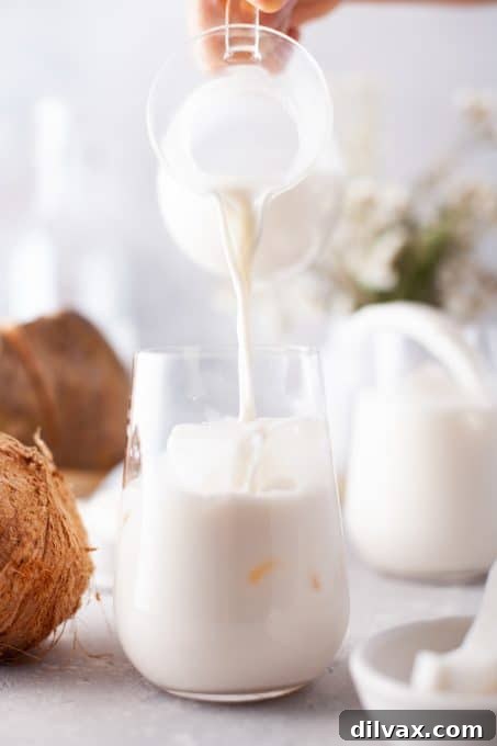 Tropical Coconut Bliss 7 A hand pouring the creamy coconut cooler from a pitcher into a glass filled with ice, ready for enjoyment.