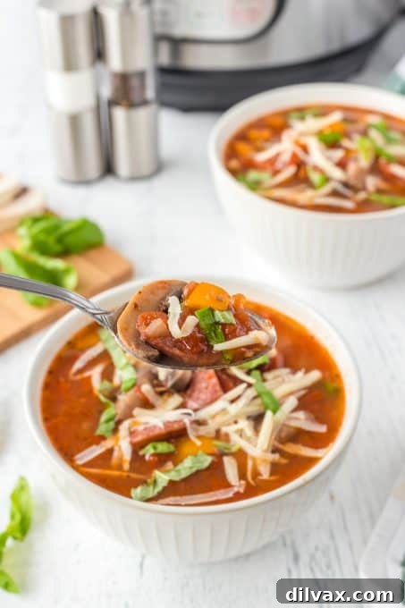 A close-up shot of Instant Pot Pizza Soup in a bowl, showing visible chunks of pepperoni, mushrooms, and melted cheese, with a spoon ready for tasting.